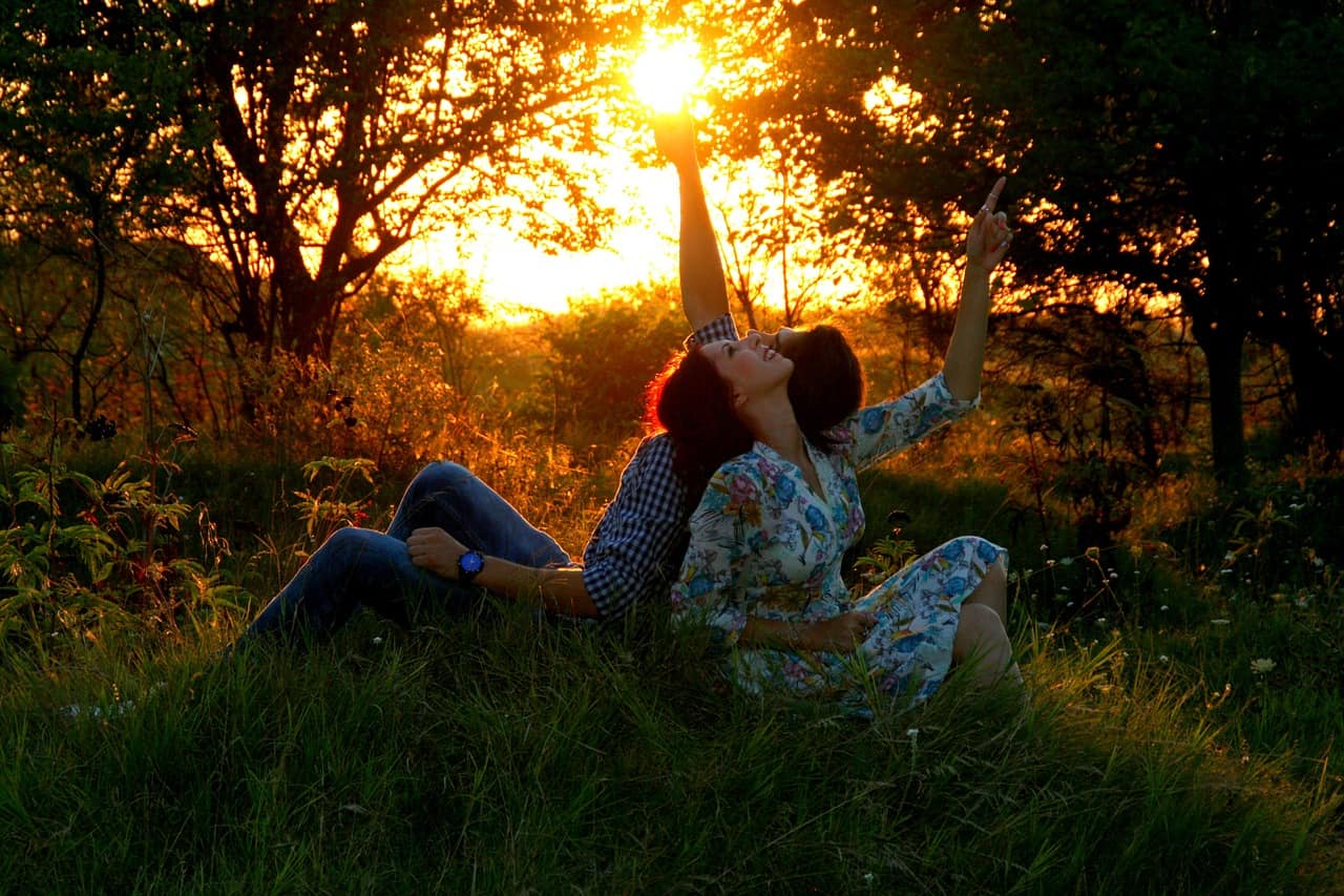 a smiling couple sitting in a field at sunset looking at the sky